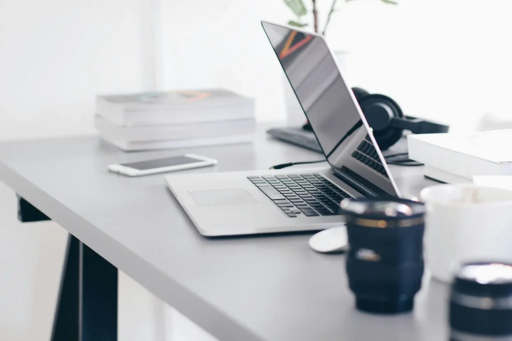 Bureau avec ordinateur portable, smartphone, souris sans fil, livres sur fond blanc.
