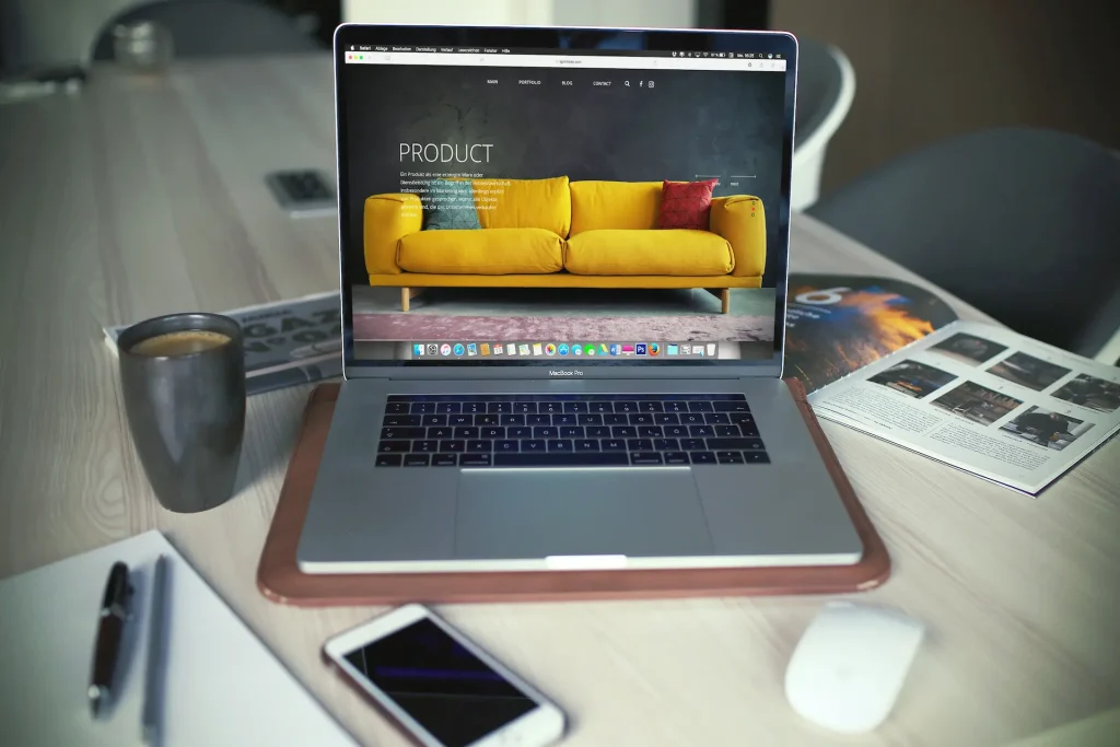 Bureau avec ordinateur portable affichant un site internet. Un smartphone, une souris sans fil, et un carnets sont posés sur le bureau.