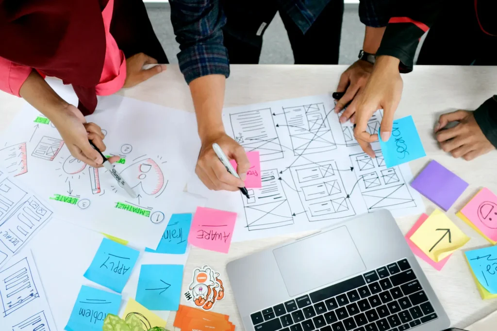 Équipe collaborant sur des wireframes UX avec post‑it et ordinateur portable