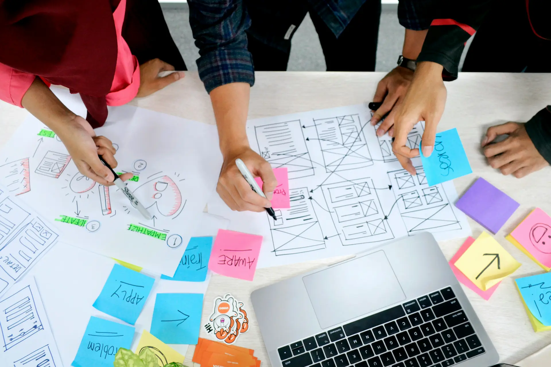Équipe collaborant sur des wireframes UX avec post‑it et ordinateur portable