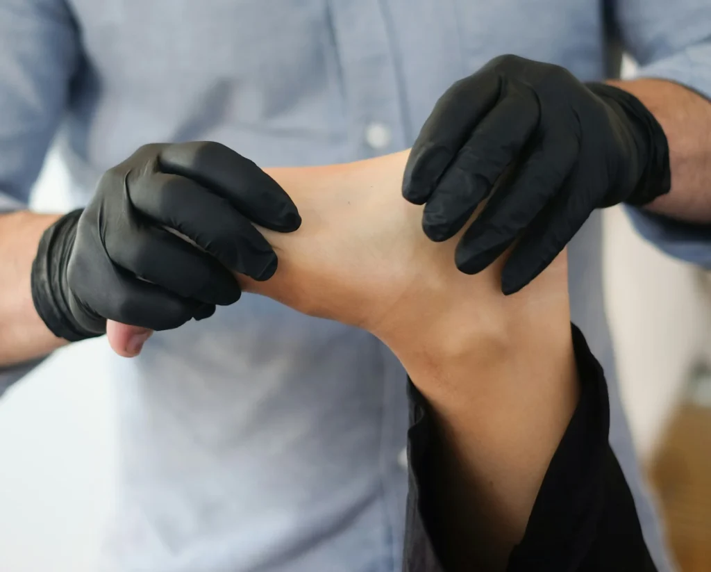 Mains gantées de noir examinant un pied en cabinet de soins