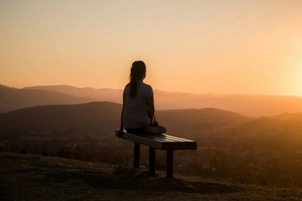 Silhouette d'une personne assise face à un paysage de collines au coucher du soleil