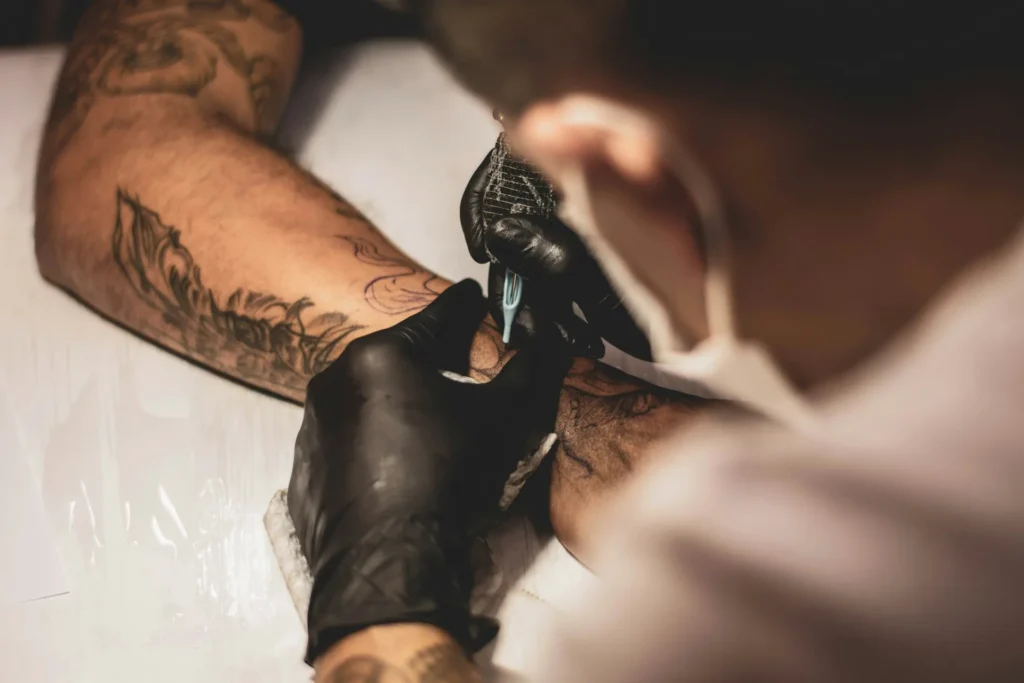 Gros plan sur une aiguille traçant un motif noir sur un avant-bras en studio