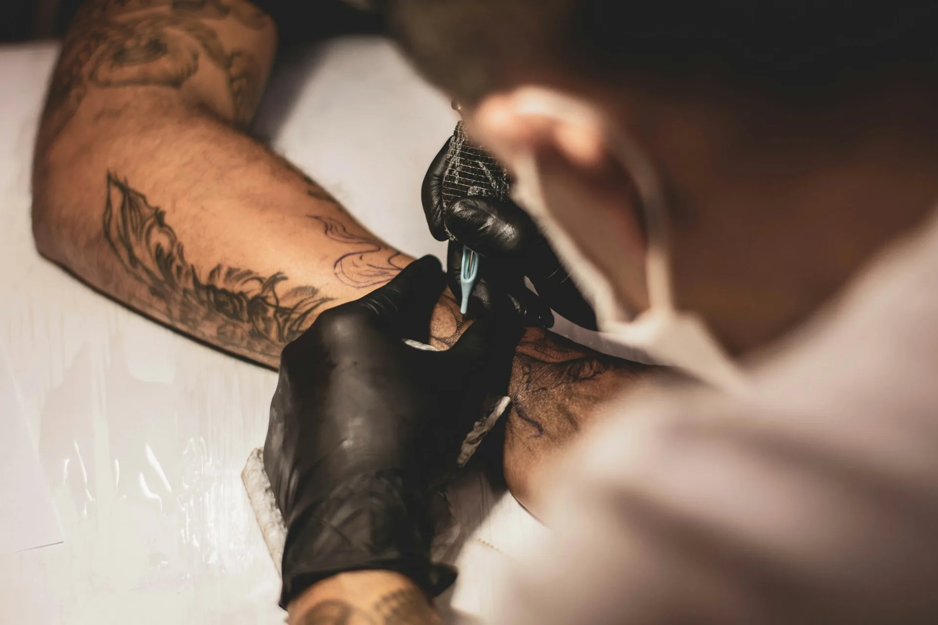 Gros plan sur une aiguille traçant un motif noir sur un avant-bras en studio
