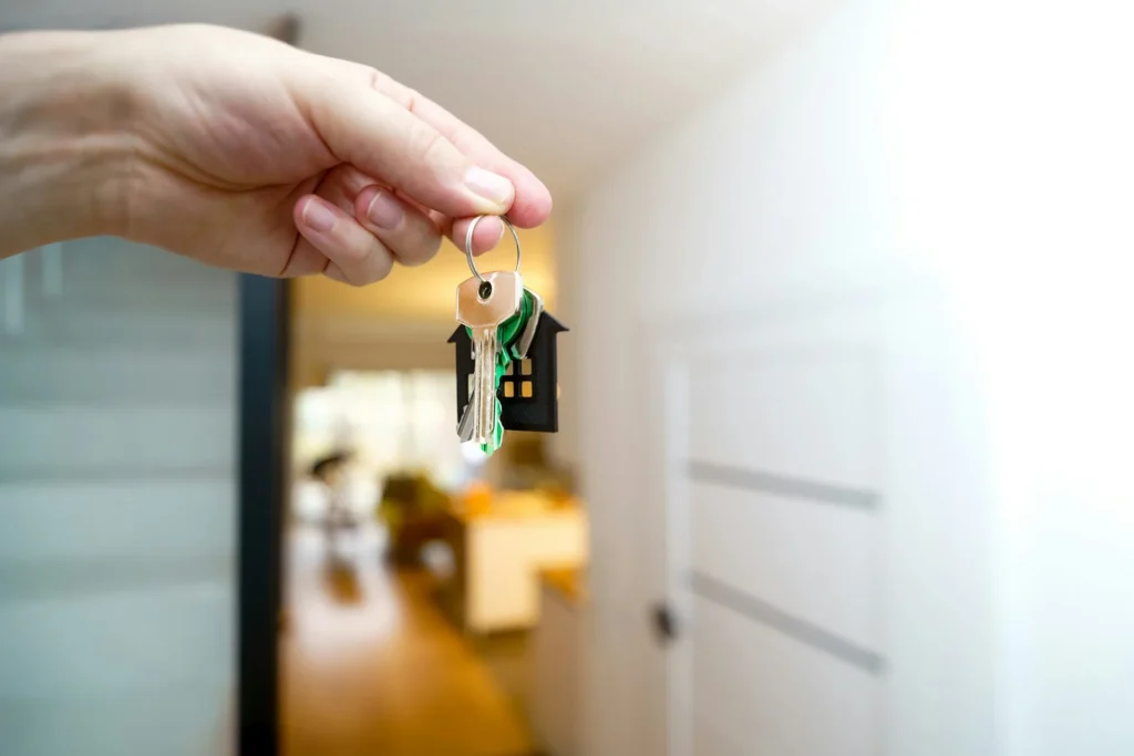 Mains tenant les clés d'une maison devant la porte d'entrée d'un nouveau logement.