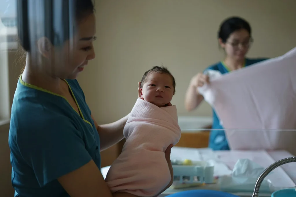 Femme portant un nouveau-né dans ses bras, ambiance maternité et accompagnement à la naissance.